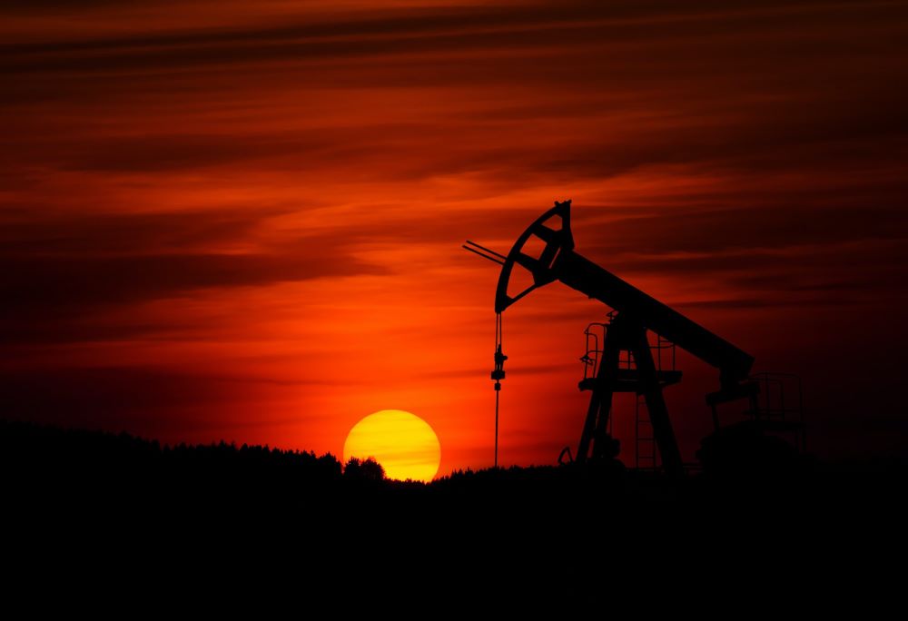 The sun sets behind a pumpjack at an oil well. (Unsplash/Zbynek Burival)