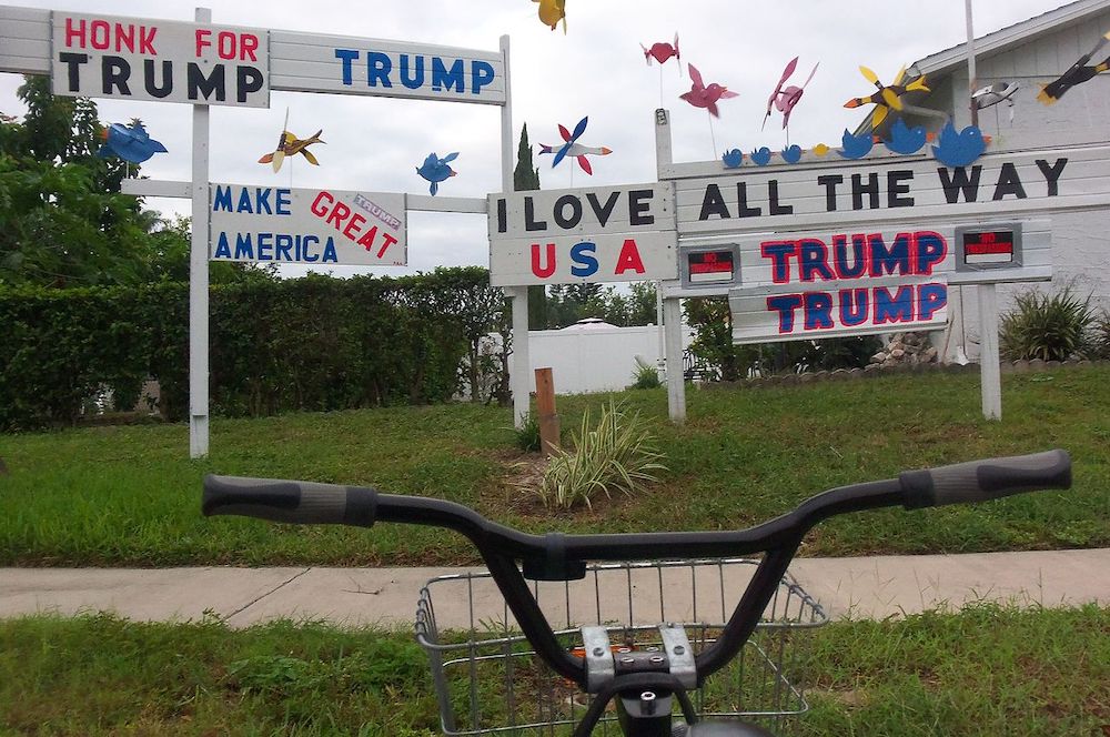 Hand painted signs in a yard with various support statements for Trump, topped with lawn ornaments