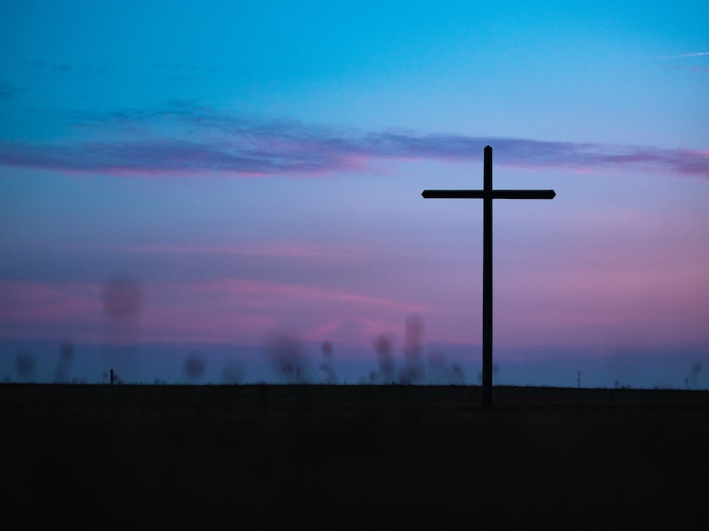 Cross seen in field during sunrise or sunset (Unsplash/Aaron Burden)