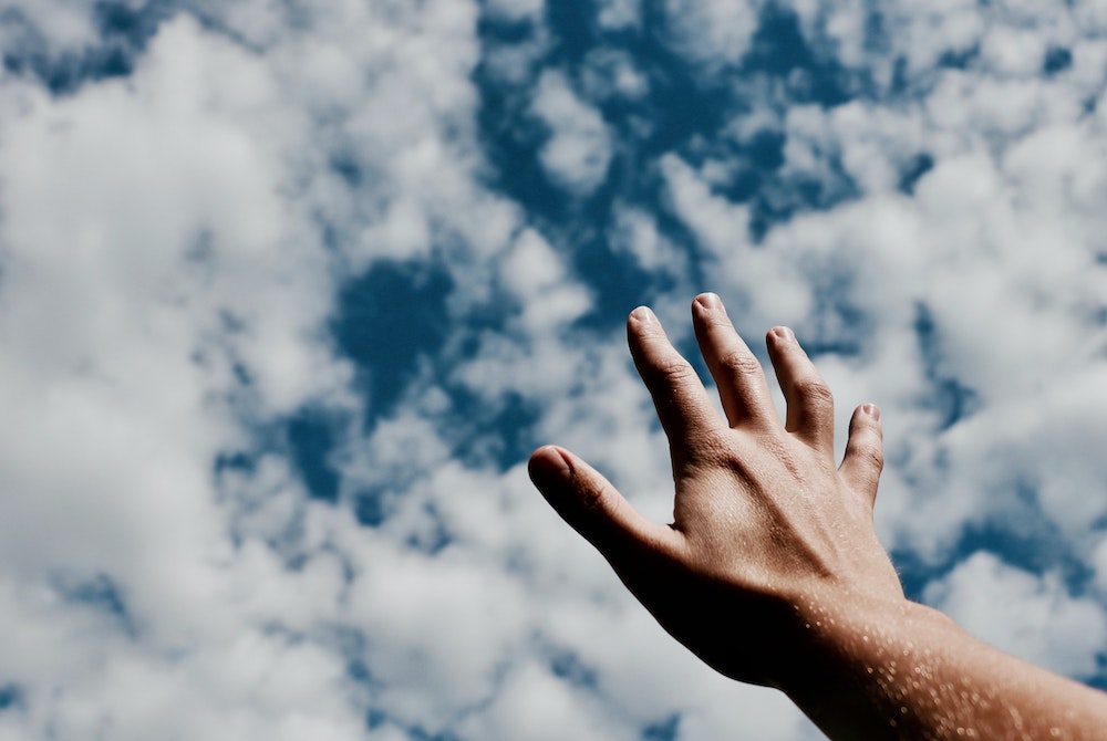 Hand reaching toward clouds in the sky (Unsplash/Jeremy Perkins)