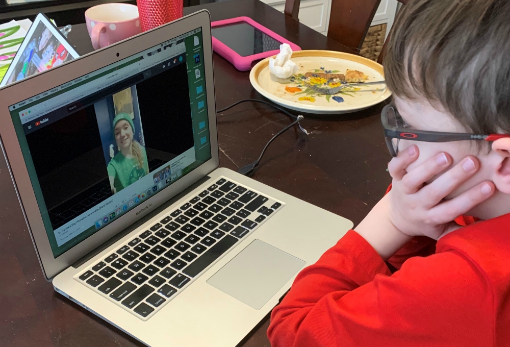 Jaxon, a second-grader at Holy Family Catholic Academy in Inverness, Illinois, watches a video from one of his teachers on a laptop at his dining room table. (Jamie Breeden)