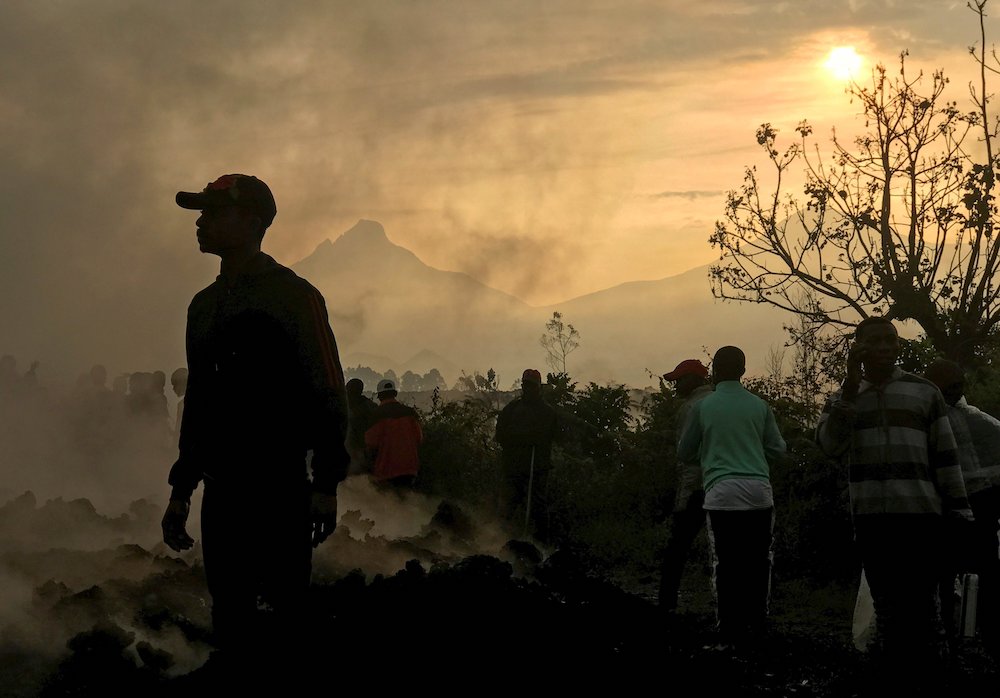 Smoke rises as residents walk near homes destroyed by lava deposited by the eruption of Mount Nyiragongo in Goma, Democratic Republic of Congo, on June 6. (CNS photo/Djaffar Al Katanty, Reuters)