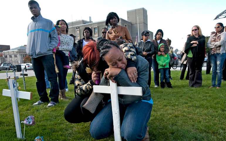 On Oct. 16, Lisa Anderson, right, weeps with her sister, Valerie, in front of a cross in memory of her son, Lateaf, in a field near City Hall commemorating homicide victims in Camden, N.J. Lateaf Anderson, 30, was shot and killed Oct. 13. (Photos by April Saul)