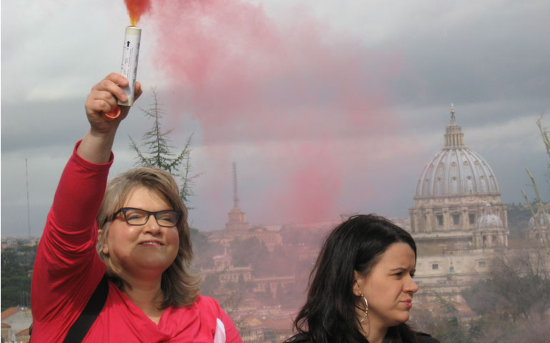 Therese Koturbash, left, holds a flare emitting pink smoke at Piazza Garibaldi in Rome March 12. Erin Saiz Hanna stands to the right, with St. Peter’s Basilica behind. (Courtesy Women’s Ordination Conference)