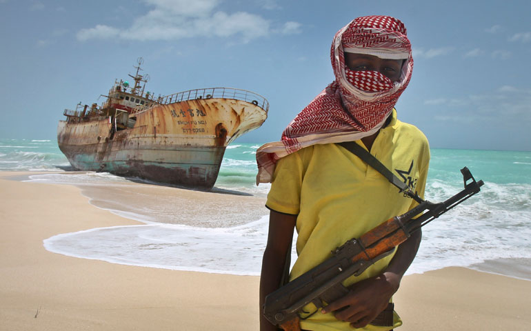 In Hobyo, Somalia, in 2012, masked Somali pirate Hassan stands near a Taiwanese fishing vessel that washed up on shore after the pirates were paid a ransom and released the crew. (AP Photo/Farah Abdi Warsameh)