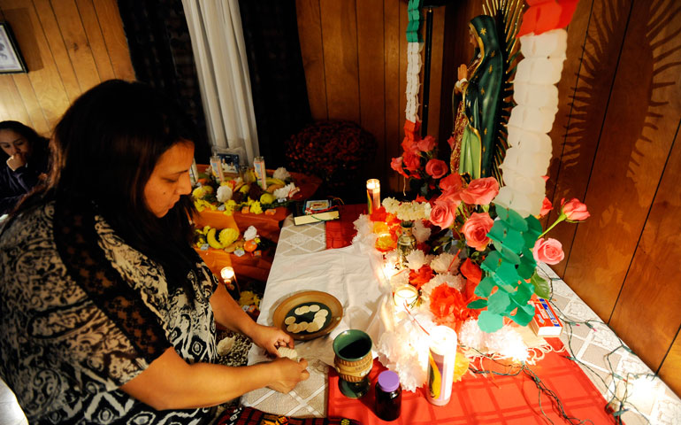 Alicia Jacobo, who hails from Mexico, prepares for Mass at her home in Brockport, N.Y., Nov. 1, All Saints’ Day. The Jacobo family built altars for both Our Lady of Guadalupe, right, and Dia de los Muertos, left. (CNS/Catholic Courier/Mike Crupi)