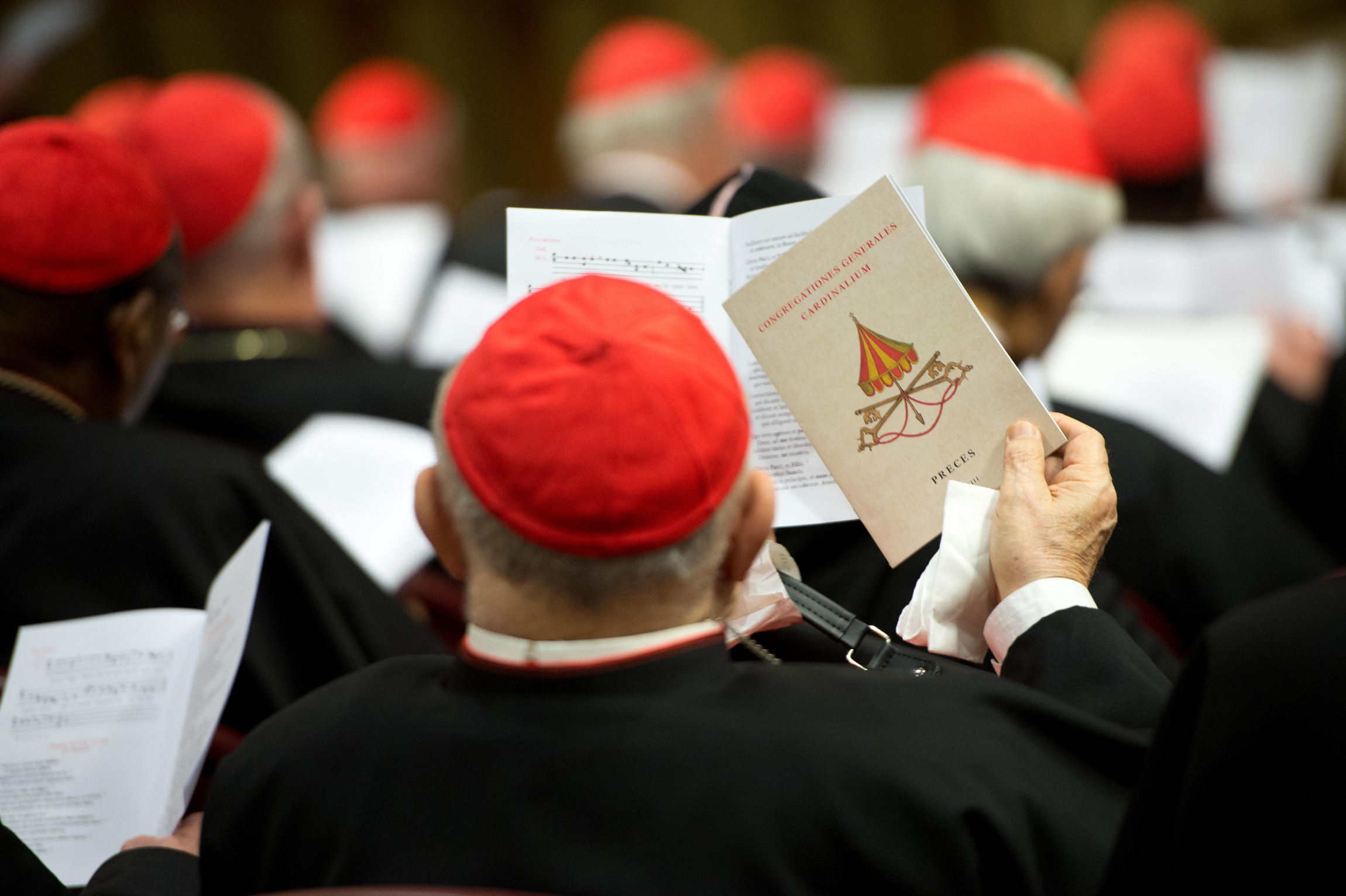 A prelate holds up a booklet emblazoned with the "sede vacante" seal as cardinals gather in synod hall at the Vatican March 7 for one of several general congregation meetings ahead of the conclave. (CNS photo/L'Osservatore Romano)