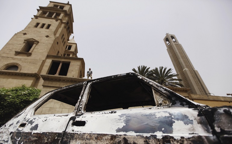An Egyptian stands on the wall of St. Mark Coptic Orthodox Cathedral April 8, as a car burned during the previous day's clashes between Muslims and Christians is pictured in the foreground. At least two people died during the clashes outside the cathedral, and more than 80 were injured. (CNS photo/Amr Abdallah Dalsh, Reuters)