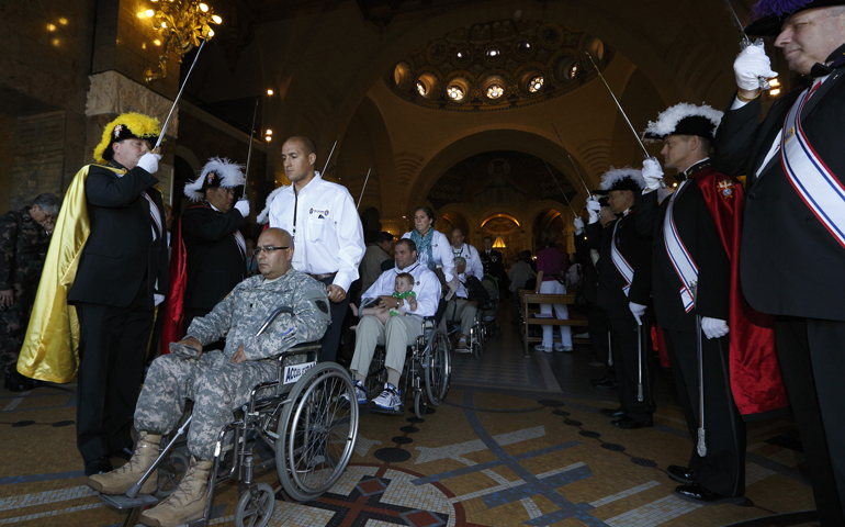 Los miembros de los Caballeros de Colón sostienen espadas mientras los soldados estadounidenses salen en sillas de ruedas después de una Misa en el Santuario de Nuestra Señora de Lourdes en el suroeste de Francia en mayo de 2014. (CNS/Paul Haring)