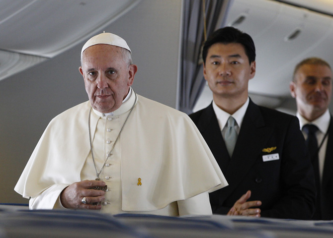 Pope Francis, still wearing a yellow pin commemorating the victims of the April 2014 ferry disaster, walks down the aisle to answer questions from journalists aboard the papal flight from Seoul, South Korea, to Rome, Aug. 18, 2014. (CNS photo/Paul Haring) 