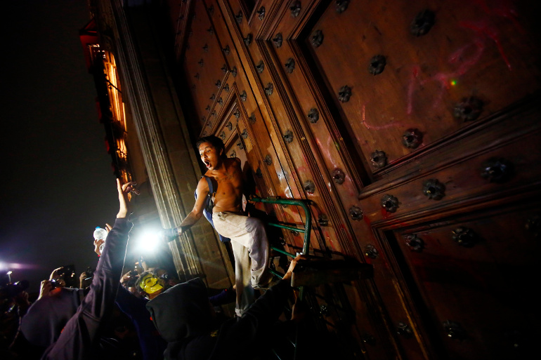 A protester climbs up a barricade leaning on the wooden door of Mexican President Enrique Pena Nieto's ceremonial palace Nov. 8, during a protest denouncing the apparent massacre of 43 trainee teachers. (CNS/Reuters/Edgard Garrido)