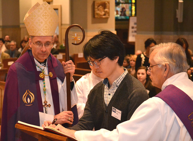 Bishop Mark L. Bartchak of Altoona-Johnstown, Pa., looks on as catechumen Dooyoung Lim signs his book of elect Feb. 22 at the Cathedral of the Blessed Sacrament in Altoona-Johnstown. (CNSMsgr. Tim Stein, Catholic Register) 