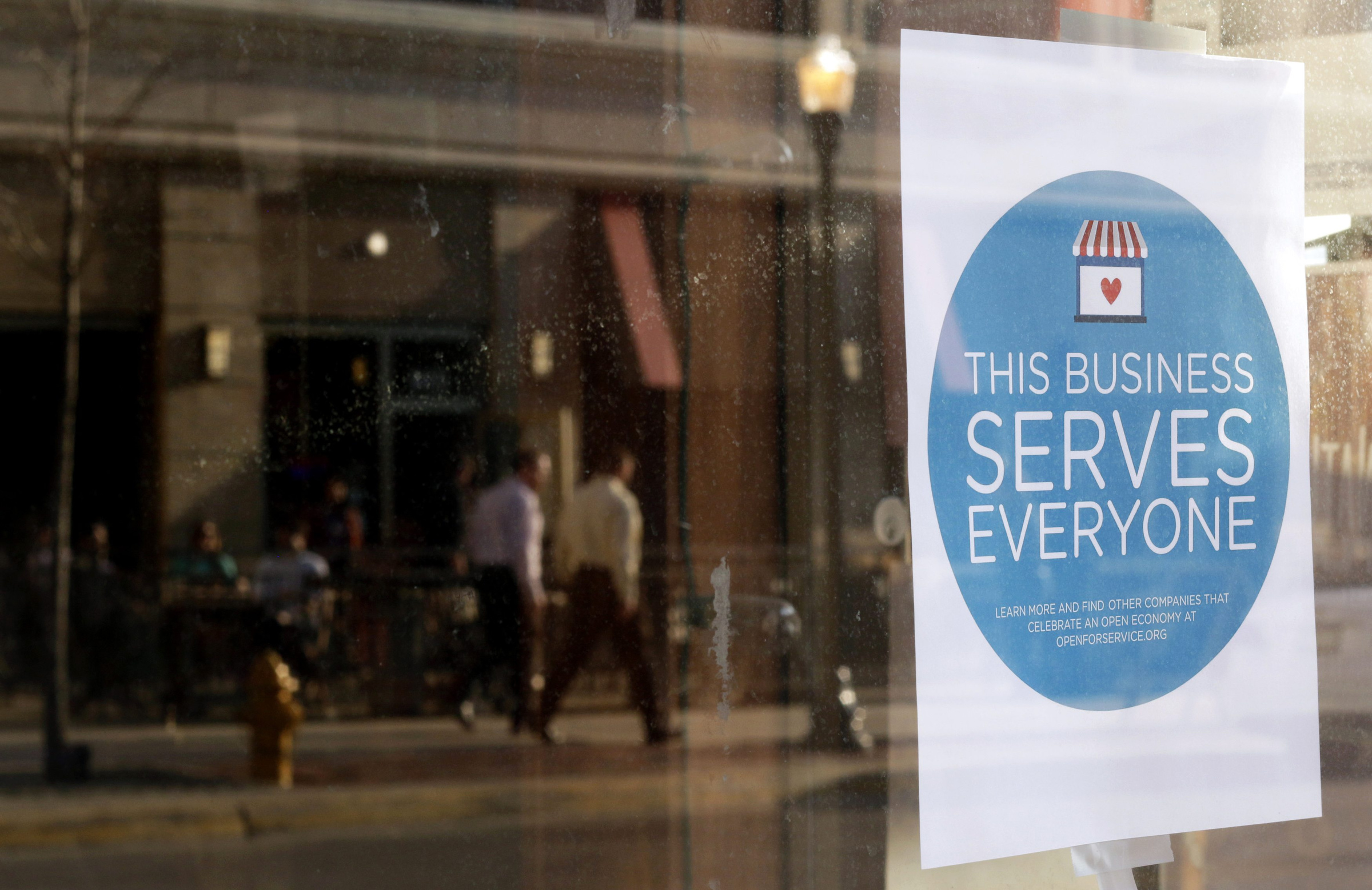A sign reading, "This business serves everyone," is seen in the window of a barbershop in downtown Lafayette, Ind., March 31. (CNS/Reuters/Nate Chute) 
