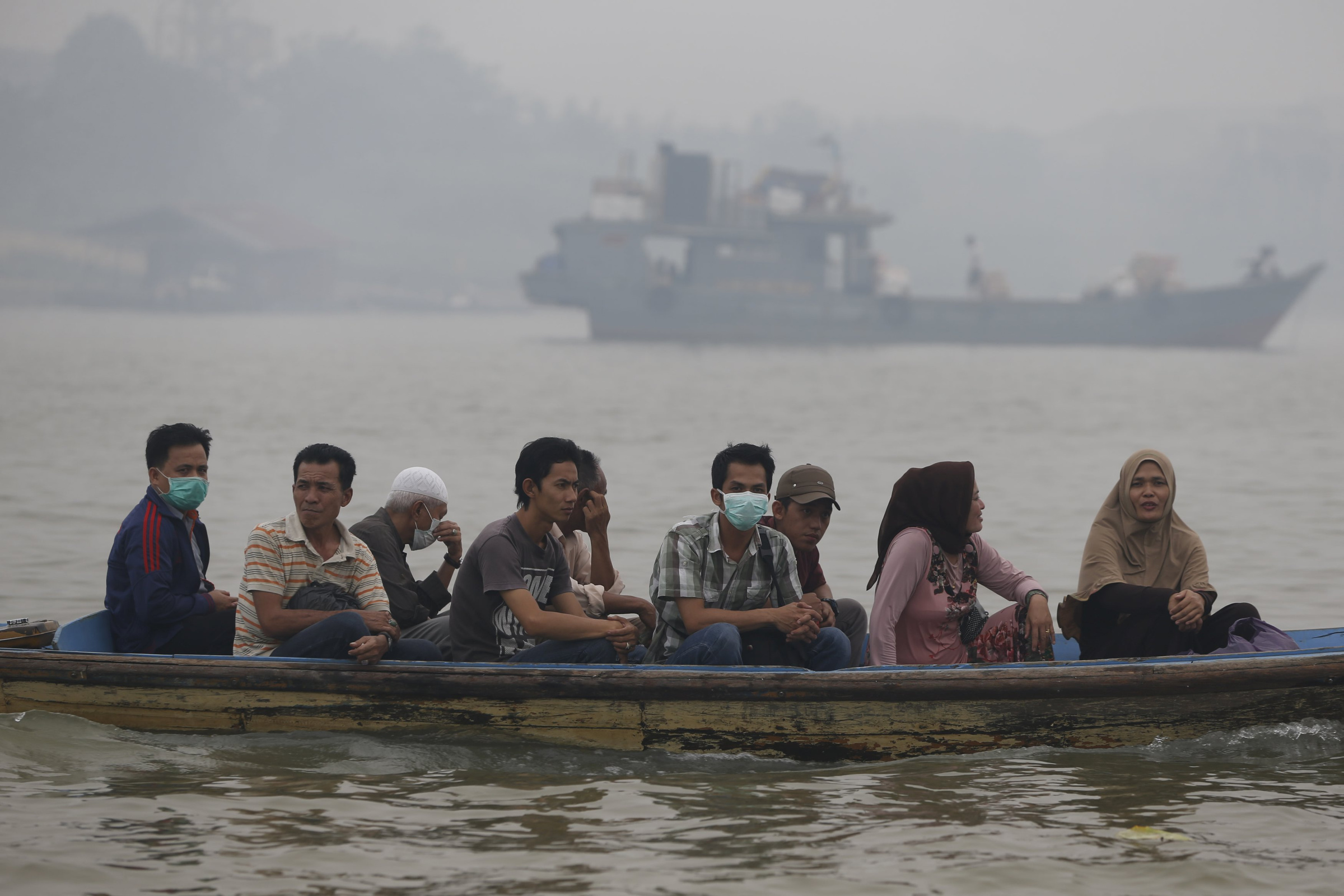 People cross the Batanghari River in Jambi, Indonesia, Sept. 14, while breathing unhealthy air caused by slash-and-burn deforestation. (CNS/Beawiharta, Reuters)