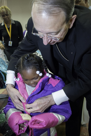 Baltimore Archbishop William E. Lori helps Tori Scott, a student in the Catholic Charities Head Start, put on a new coat donated by the Knights of Columbus Nov. 30. (CNS/Olivia Obineme, Catholic Review)
