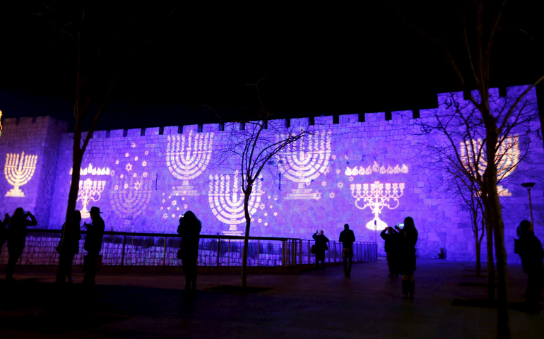 People walk past images of Menorahs projected on a wall surrounding the Old City of Jerusalem Dec. 8. (CNS/Ammar Awad, Reuters)