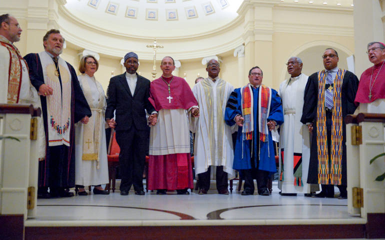 Baltimore Archbishop William E. Lori, center, and area faith leaders, join hands in song to close the April 25 interfaith prayer service for peace at the Basilica of the National Shrine of the Assumption of the Blessed Virgin Mary in Baltimore. The service marked the anniversary of the riots that spread through Baltimore April 27, 2015, after the funeral of Freddie Gray Jr., who died of injuries suffered while in police custody. (CNS photo/Kevin J. Parks, Catholic Review)