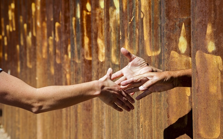 Two hands reach out from the U.S. side of the border fence to shake the hand of a person on the Mexican side Oct. 8 during immigration rallies in Nogales, Ariz., and in Nogales in the Mexican state of Sonora. Activists protested what they say is an increasing militarization of the border. (CNS/Jim West)