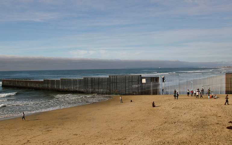 People in Tijuana, Mexico, stand next to a wall separating Mexico and the United States Dec. 10. (CNS/Jorge Duenes, Reuters)