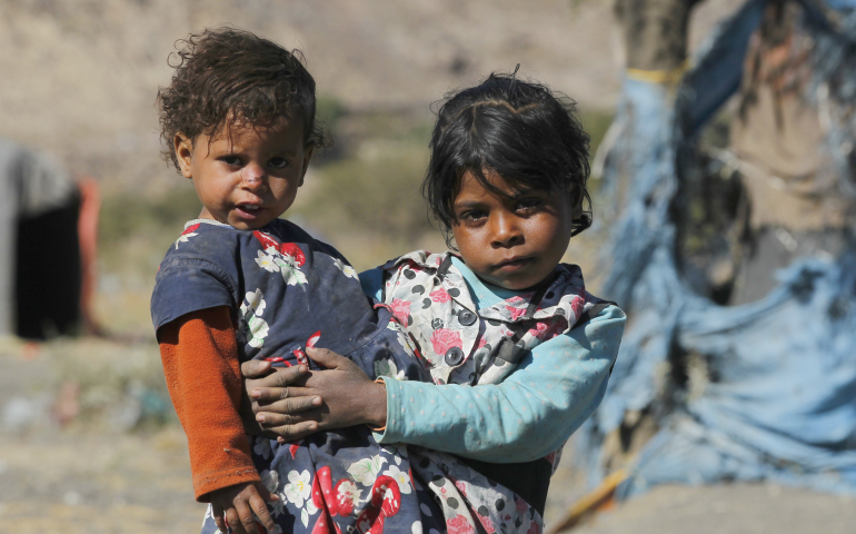 A girl holds her sister near a makeshift shelter Dec. 6 at a camp for displaced people on the outskirts of Sana'a, Yemen. "Creating a Culture of Encounter" is the theme of 2017's National Migration Week, an annual observance the U.S. Catholic bishops began over 25 years ago. (CNS photo/Yahya Arhab EPA)