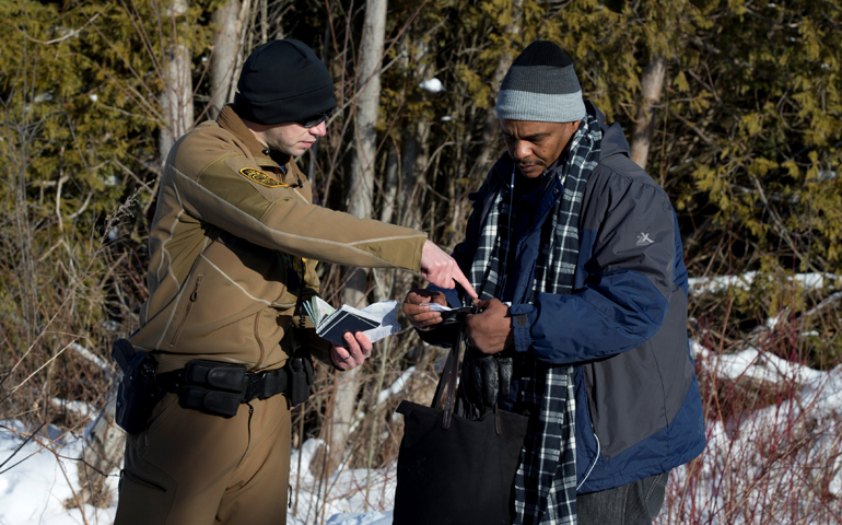 A man who claimed to be from Sudan has his and his family's passports checked by a U.S. border patrol officer Feb. 17 in Champlain, N.Y., at the U.S.-Canada border. (CNS/Christinne Muschi, Reuters)