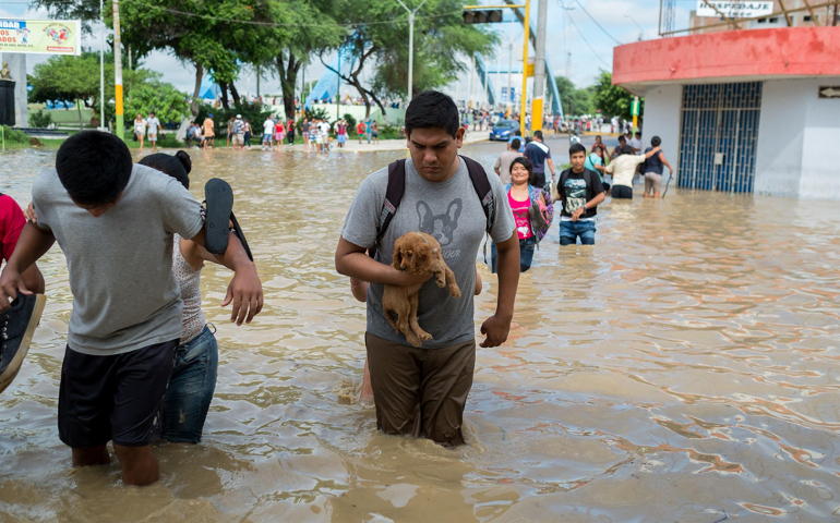 People cross a street flooded by the Piura River on March 27 in Peru. (CNS photo / EPA / Edwin Zapata Alvarado) 