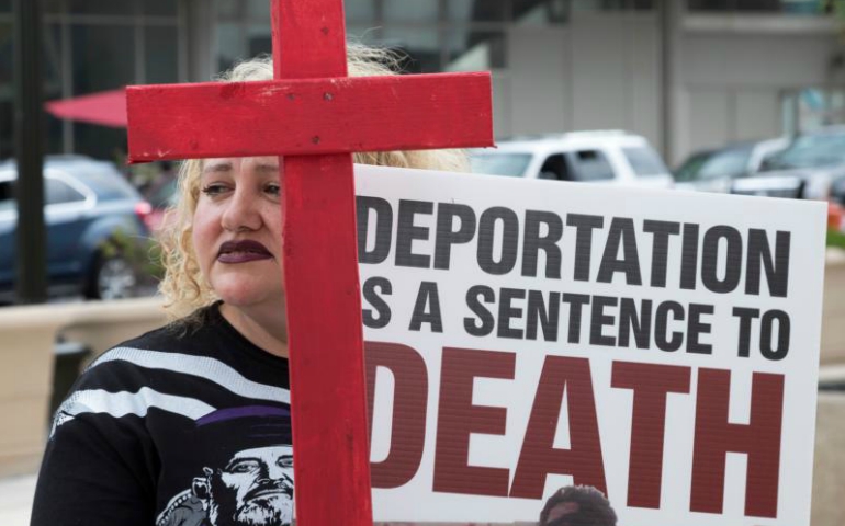 A woman holds a sign and cross as members of the local Chaldean community demonstrate June 16 outside the Patrick V. McNamara Federal Building to protest the arrest and detention of more than 100 Chaldean Christians from the Detroit area. (CNS/Jim West)