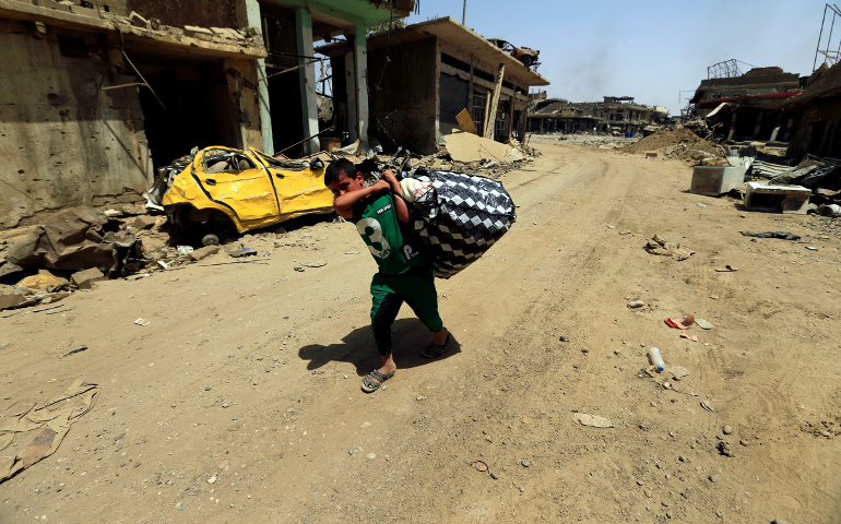 A boy carries his belongings in Mosul, Iraq, July 23. Some Iraqi Christians who are making their slow return to ancestral lands say it will take time to rebuild their lives and trust of those who betrayed them. (CNS/Thaier Al-Sudani, Reuters)