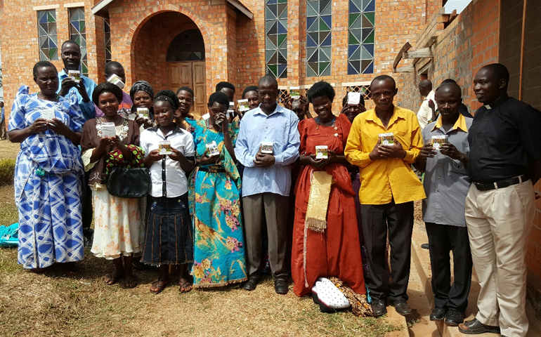 Fr. Mathias Mulumba standing with parents who received solar lamps for their children to study at home. (Provided photo)
