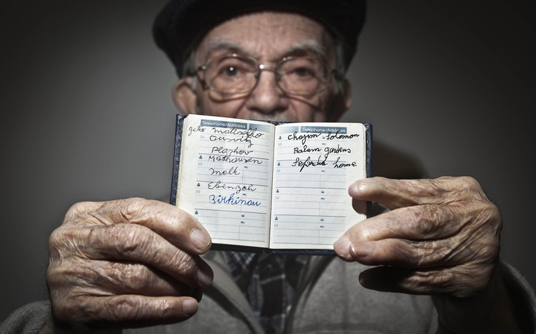 Holocaust survivor Hy Abrams, 90, poses for a portrait Jan. 15 in the Brooklyn borough of New York with a book that documents all the different concentration camps he was held in during World War II. Abrams was taken at age 20 by German Nazi soldiers and separated from his mother, father, brother and three sisters. (CNS/Reuters/Carlo Allegri)