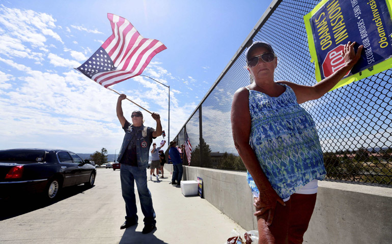 Protesters Mark Connors and Nancy Greyson wave flags and signs saying "Stop Obama's Invasion" July 19 as motorists go by on a highway overpass in Murrieta, Calif. (CNS/Reuters/Sandy Huffaker)