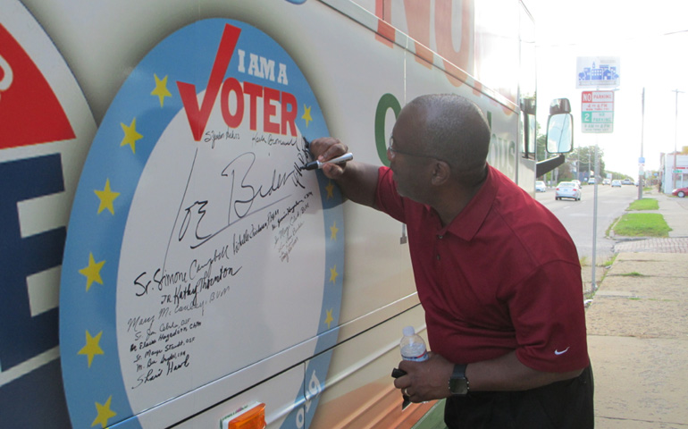 Will Butts, one of the drivers for Nuns on the Bus, signs the bus in Des Moines, Iowa, Sept. 17. (NCR photo/Jan Cebula)