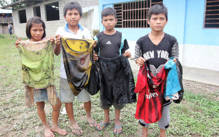 Awajun children in the community of Nazareth, at the confluence of the Chiriaco and Maranon rivers in northern Peru, show the clothes they wore -- with no protective equipment -- to scoop oil out of water near their community after a pipeline break in February. (CNS photo/Barbara Fraser) 