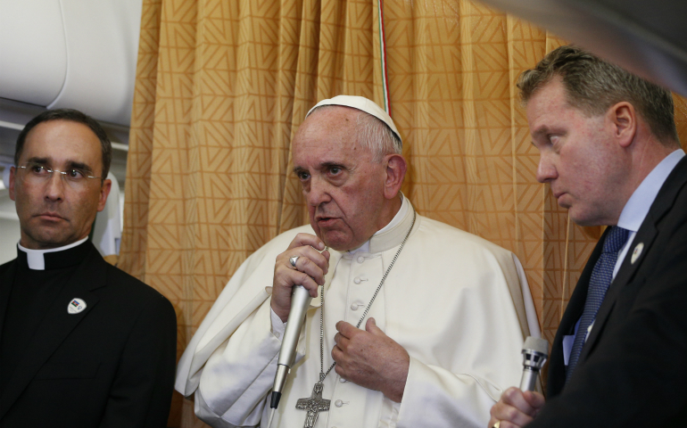 Pope Francis responds to a reporter's question about the U.S. presidential election aboard his flight from Baku, Azerbaijan, to Rome Oct. 2. At left is Father Mauricio Rueda Beltz, papal trip planner; at right is Greg Burke, the new Vatican spokesman. (CNS photo/Paul Haring)
