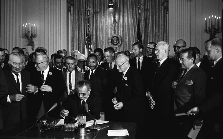 U.S. President Lyndon B. Johnson signs the Civil Rights Act into law July 2, 1964, as the Rev. Martin Luther King Jr. and others look on. (CNS/Cecil Stoughton, courtesy LBJ Library)