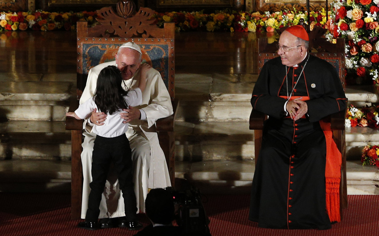 Pope Francis embraces a girl during a meeting with representatives of civil society Tuesday in the Church of St. Francis in Quito, Ecuador. At right is Ecuadorean Cardinal Raul Vela Chiriboga. (CNS/Paul Haring)
