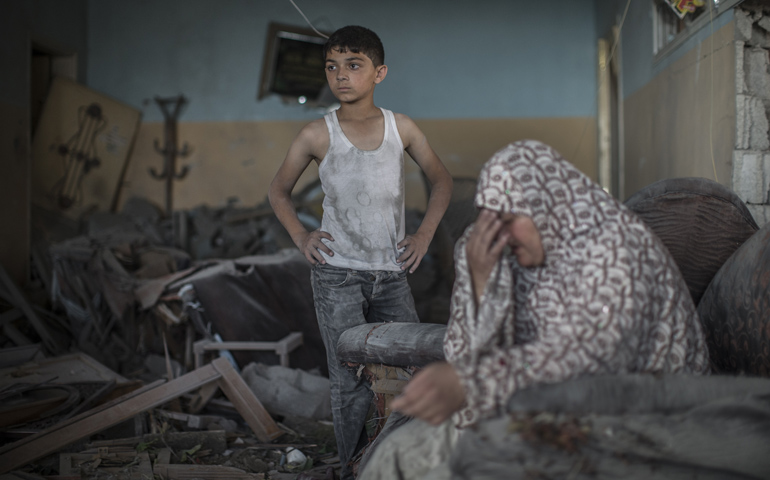 A Palestinian woman cries while sitting next to her son Thursday in their Gaza City house, which was badly damaged in an overnight airstrike by Israeli Defense Forces. (CNS/EPA/Oliver Weiken)