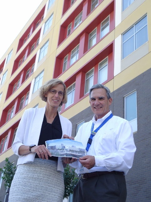 Twin Cities Catholic Charities CEO Tim Marx, right, and Tracy Berglund, senior director of housing stability with Twin Cities Catholic Charities, stand in front of Higher Ground in Minneapolis, holding an artist's conception of the Higher Ground shelter being built in St. Paul. (NCR photo/Joe Winter)