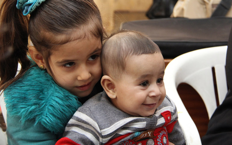 Rawan Al Kurdi, 5, holds her brother, Ahmad, at the Mafraq Refugee Center and Latin School in Mafraq, Jordan, in October 2014. The Syrian children fled to Jordan with their mother in 2012. (CNS/Catholic Relief Service/Kim Pozniak)