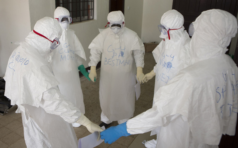 Health workers in protective equipment pray at the start of their shift before entering the Ebola treatment center Sept.30 in Monrovia, Liberia. (CNS/Reuters/WHO/Christopher Black)
