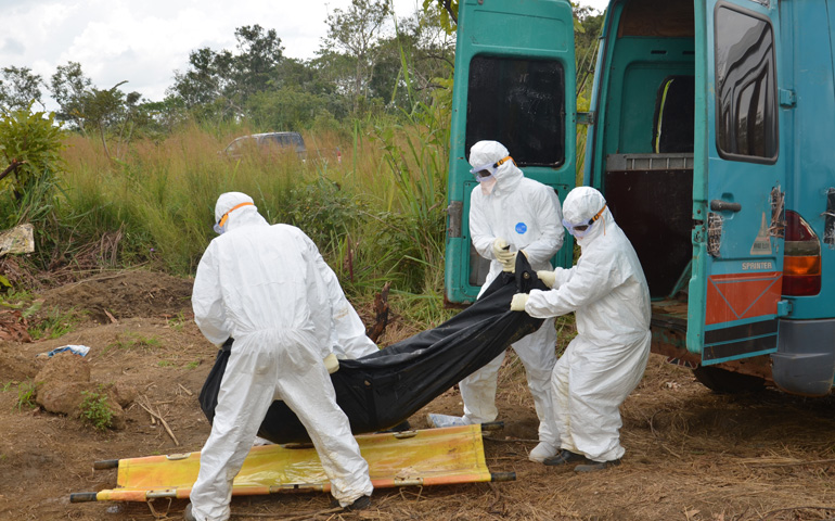 Health workers in protective gear take a body bag containing the highly contagious body of an Ebola victim out of a vehicle in preparation for burial at a cemetery in the Port Loko district in northern Sierra Leone. (CNS/ Courtesy Catholic Relief Services/Michael Stulman)