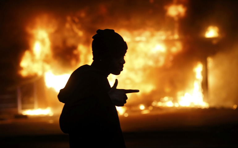 A man walks past a burning building during rioting Monday in Ferguson, Mo., after a grand jury returned no indictment in the Aug. 9 shooting death of Michael Brown in the St. Louis suburb. (CNS/Reuters/Jim Young)