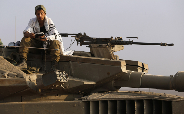 An Israeli soldier prays atop a tank Wednesday near the border with the Gaza Strip. (CNS/Reuters/Baz Ratner)