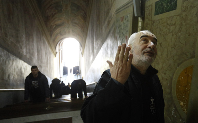 Passionist Fr. Francesco Guerra talks about artwork above the Holy Stairs as people pray on their knees March 10 at the Pontifical Sanctuary of the Holy Stairs in Rome. (CNS/Paul Haring)