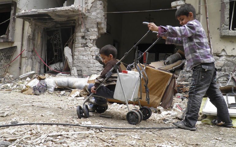 A boy pushes a stroller holding water and another child past destroyed buildings Sunday in the besieged area of Homs, Syria. (CNS/Reuters/Thaer Al Khalidiya)