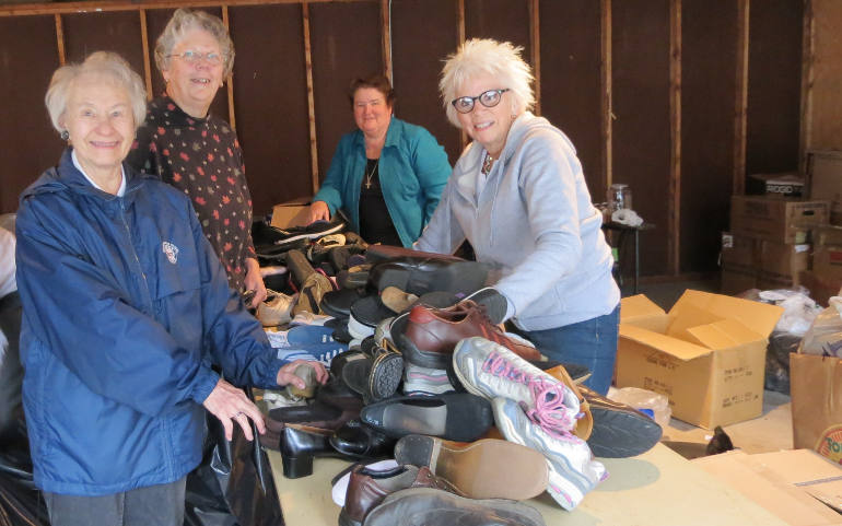 Donated shoes pile up on a table in October at the Sisters of Notre Dame Provincial Center, in Toledo, Ohio, waiting to be counted and bagged. From left, Rita Konecki, Dorothy Wodrich, Notre Dame Sr. Frances Marie Penwell and Linda Schlachter. (Teri Bockstahler)