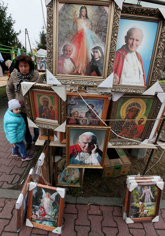 A woman and a child walk past a vendor offering portraits of St. John Paul II during a parish fair in the town of Lomianki, Poland, Nov. 9, 2014. (AP Photo/Czarek Sokolowski)