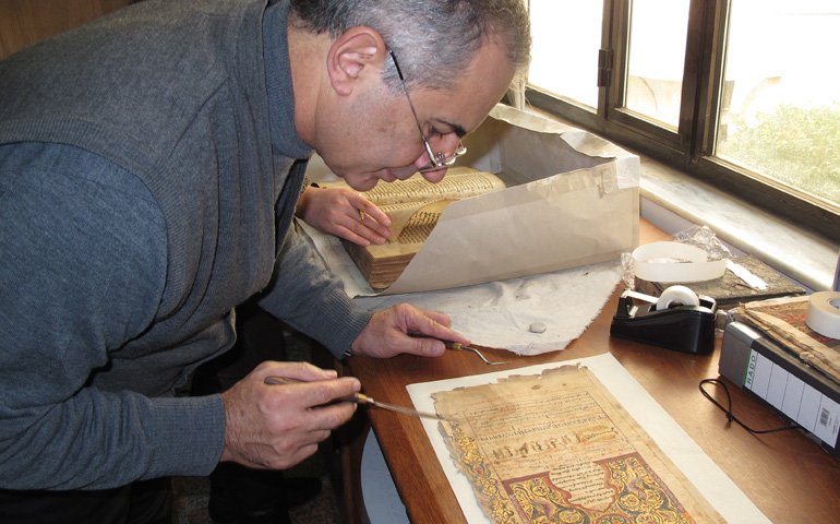 Dominican Fr. Najeeb Michaeel works on a manuscript at his restoration laboratory in Qaraqosh, Iraq, prior to Aug. 6. (CNS/Courtesy of Centre Numerique des Manuscrits Orientaux) 