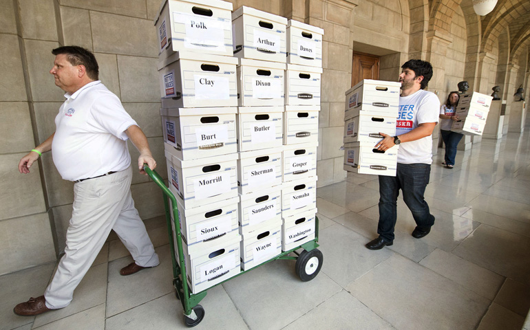 On July 3, 2014, Rodney Vicek (left) of Lincoln, Neb., leads a group hauling boxes that contain some of the signed petitions to raise the state's minimum wage, enough to get the measure on the ballot in November, when it passed. (AP Photo/Lincoln Journal Star/Francis Gardler)
