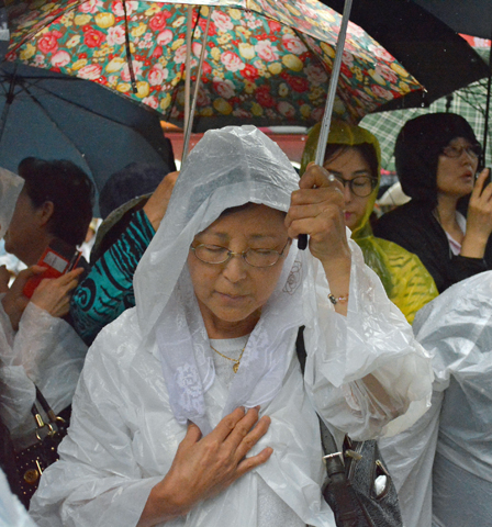 A woman prays with others in the rain outside Myongdong Cathedral in Seoul, South Korea, on Monday as Pope Francis celebrates a Mass for peace and for the reconciliation of North and South Korea inside. (CNS/Simone Orendain)